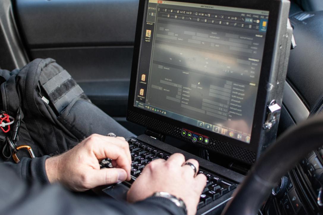 Police office typing on a laptop in a cop car.