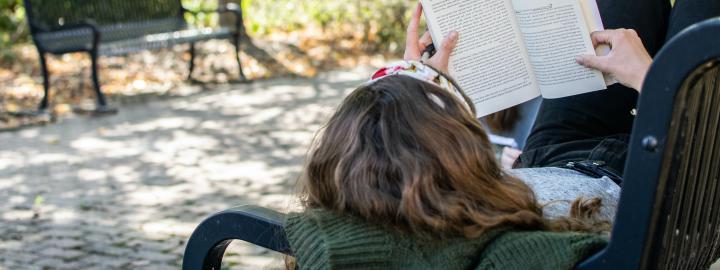 Student laying on a bench reading a book.